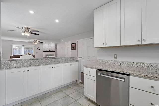 kitchen with a large fireplace, dishwasher, light stone counters, white cabinets, and a textured ceiling