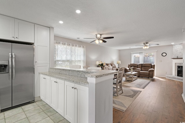 kitchen with a peninsula, a fireplace, stainless steel fridge with ice dispenser, and white cabinetry