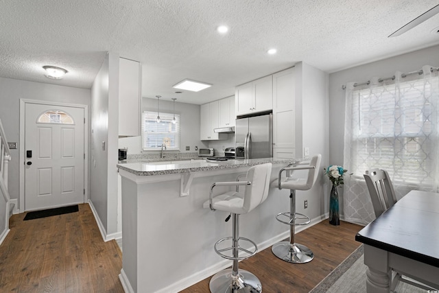 kitchen with dark wood-type flooring, under cabinet range hood, stainless steel appliances, white cabinets, and light stone countertops