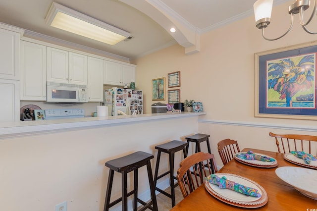 kitchen with white appliances, white cabinetry, light countertops, a kitchen bar, and crown molding