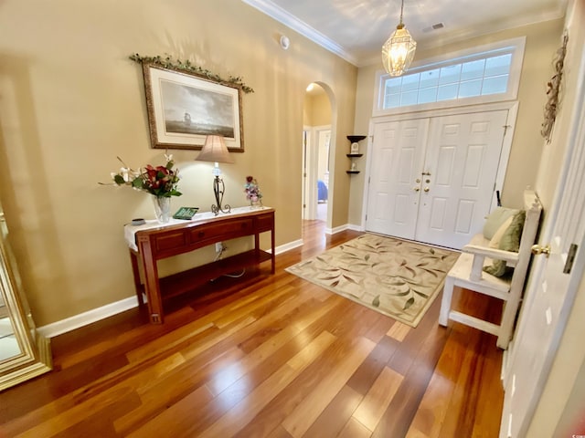 entrance foyer featuring arched walkways, crown molding, visible vents, wood finished floors, and baseboards