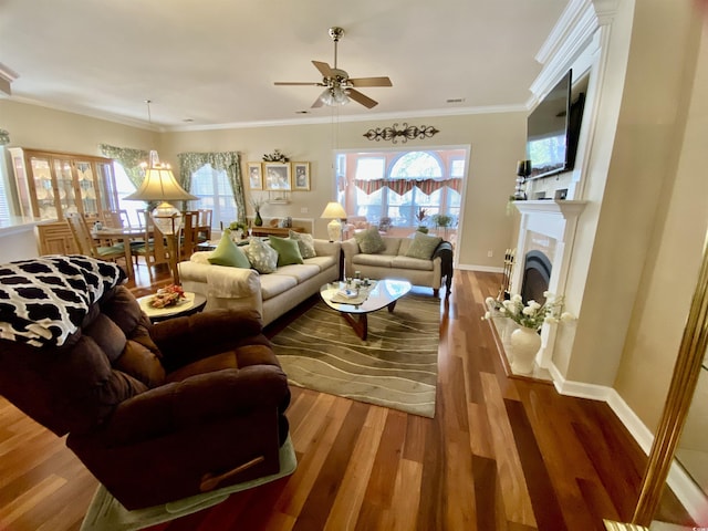 living room with crown molding, a fireplace with raised hearth, a ceiling fan, wood finished floors, and baseboards