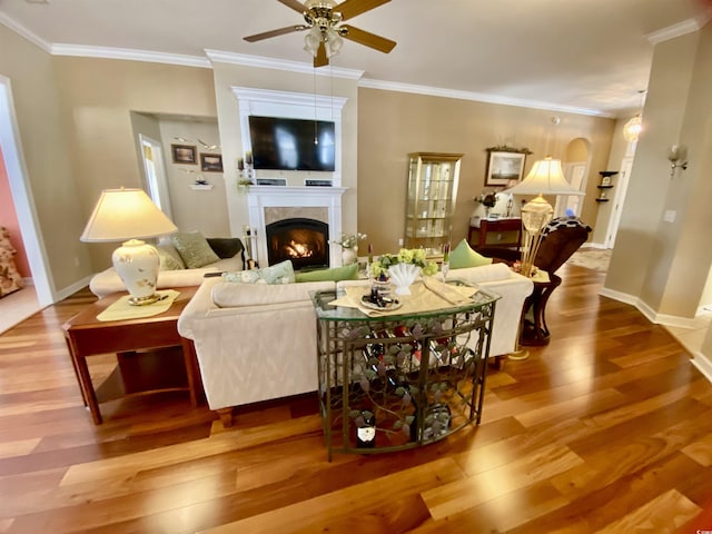 living area with a warm lit fireplace, ornamental molding, wood finished floors, and baseboards