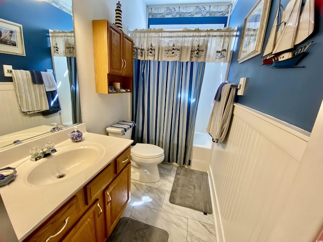 full bath featuring toilet, marble finish floor, vanity, and wainscoting