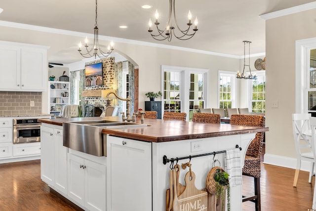 kitchen with a notable chandelier, dark wood-type flooring, ornamental molding, stainless steel oven, and butcher block countertops