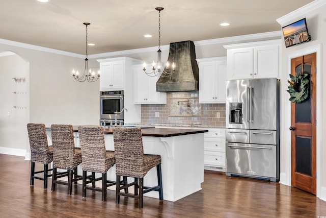 kitchen with a sink, appliances with stainless steel finishes, custom exhaust hood, tasteful backsplash, and a center island with sink