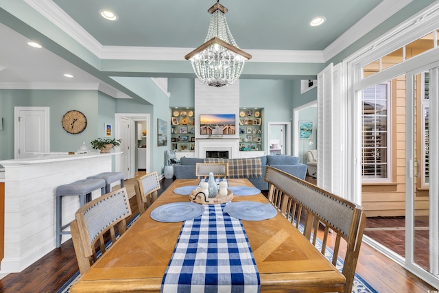 dining space featuring a fireplace, recessed lighting, an inviting chandelier, ornamental molding, and hardwood / wood-style floors