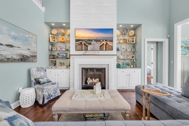 living area with built in features, a glass covered fireplace, a high ceiling, and wood finished floors