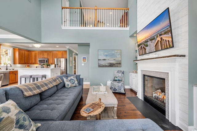 living room featuring dark wood-style flooring, crown molding, a high ceiling, a fireplace with flush hearth, and baseboards