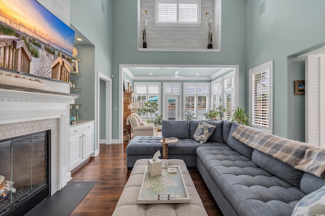 living area with a high ceiling, dark wood-style flooring, a glass covered fireplace, and visible vents