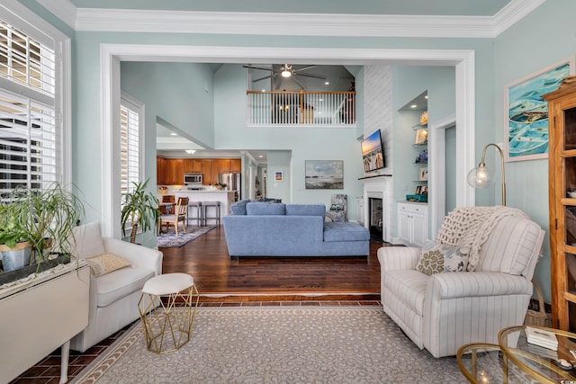 living area with a fireplace, crown molding, a towering ceiling, and wood finished floors