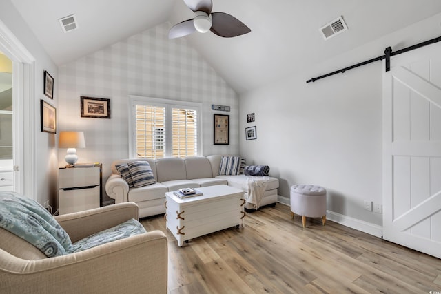 living room featuring a barn door, light wood-style flooring, visible vents, baseboards, and a ceiling fan