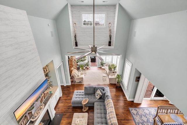 living room featuring ceiling fan, a fireplace, a high ceiling, and dark wood finished floors