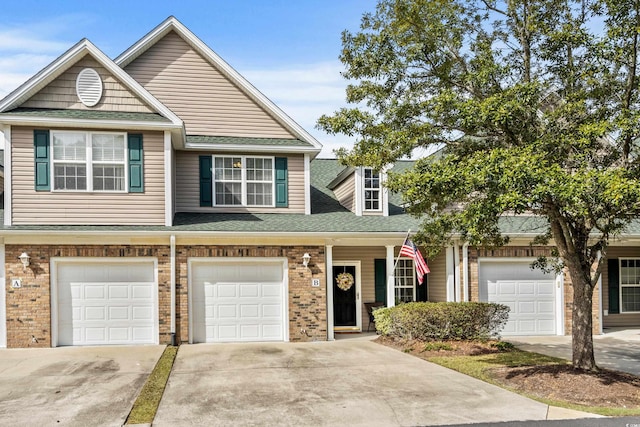 view of property with driveway, a shingled roof, a garage, and brick siding