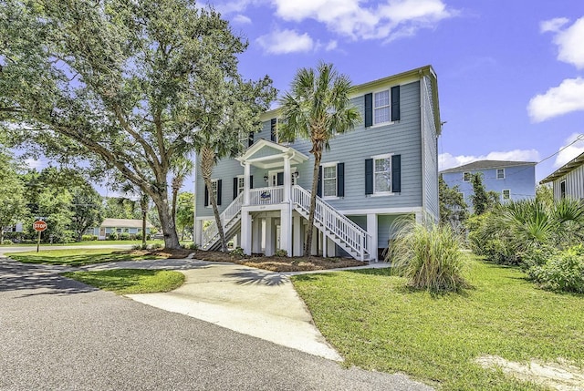 raised beach house with a front yard, covered porch, driveway, and stairway