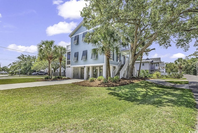 raised beach house with stairs, a carport, a front lawn, and concrete driveway