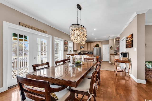 dining room featuring french doors, an inviting chandelier, ornamental molding, light wood-style floors, and baseboards