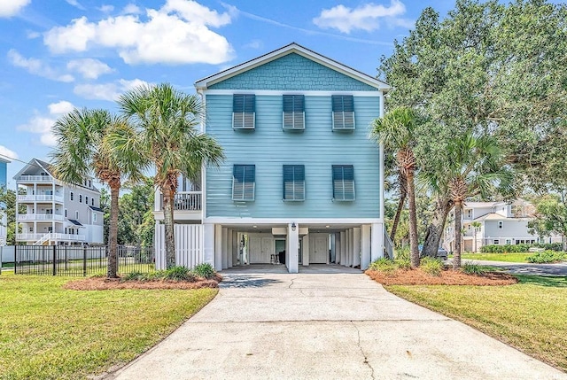 coastal inspired home featuring driveway, fence, a carport, and a front yard