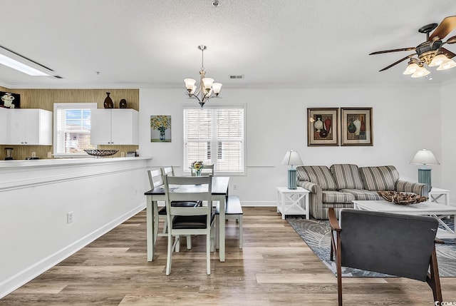 dining space with visible vents, ornamental molding, wood finished floors, a textured ceiling, and ceiling fan with notable chandelier