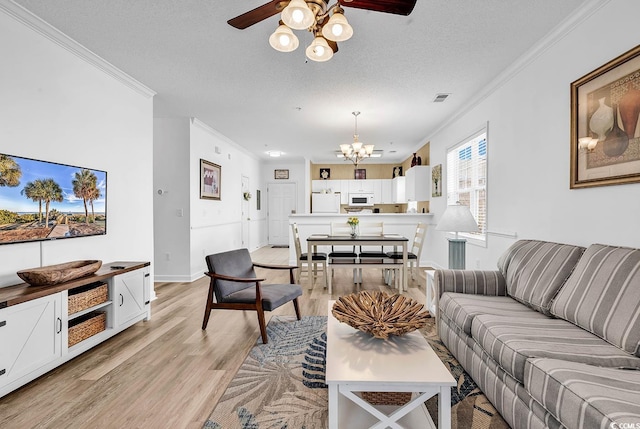 living area featuring visible vents, light wood-style flooring, ornamental molding, a textured ceiling, and ceiling fan with notable chandelier