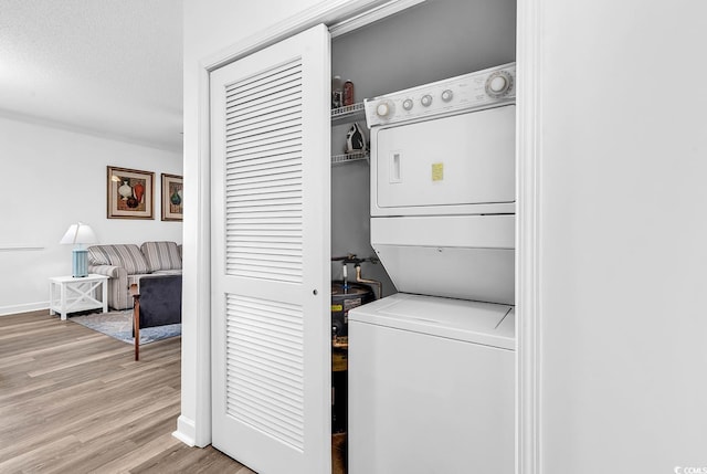 laundry area with a textured ceiling, laundry area, baseboards, stacked washing maching and dryer, and light wood finished floors