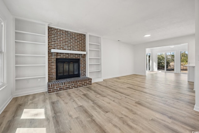 unfurnished living room with a brick fireplace, built in shelves, baseboards, and wood finished floors