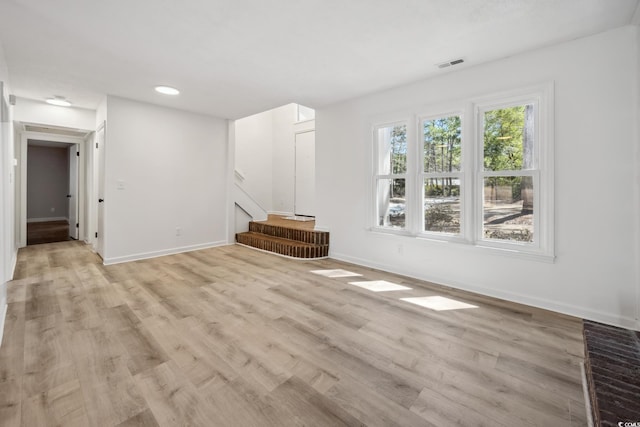 unfurnished living room with light wood-type flooring, visible vents, baseboards, and stairs