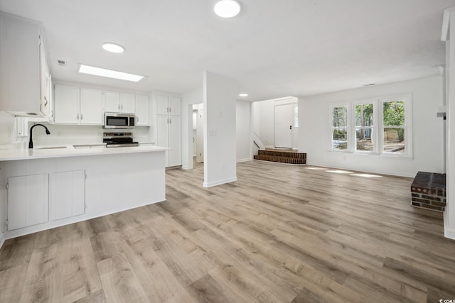 kitchen featuring a skylight, light countertops, appliances with stainless steel finishes, open floor plan, and a peninsula