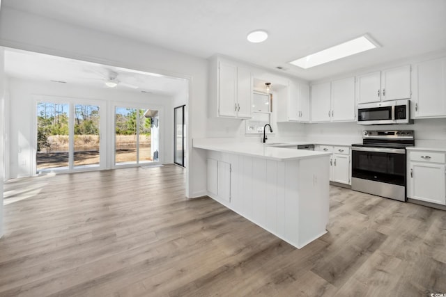 kitchen with a peninsula, a skylight, a sink, light countertops, and appliances with stainless steel finishes