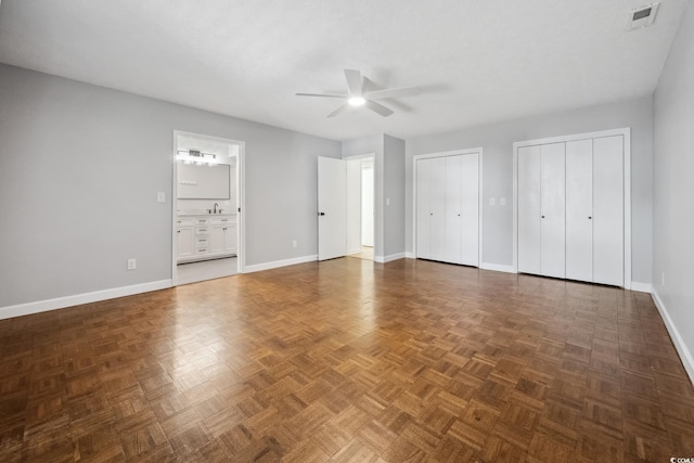 unfurnished bedroom featuring ensuite bath, two closets, visible vents, and baseboards
