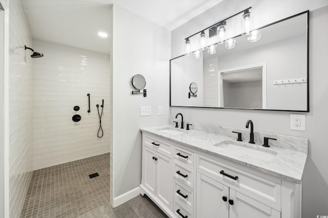 full bath with double vanity, baseboards, a sink, and tiled shower