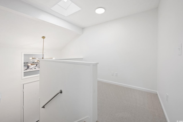 corridor featuring vaulted ceiling with skylight, baseboards, carpet flooring, and an upstairs landing