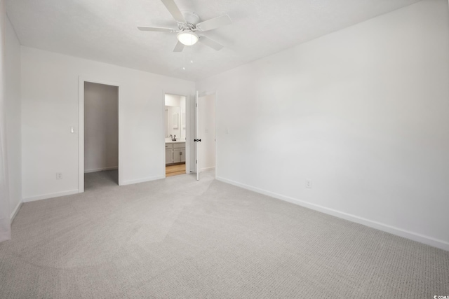 unfurnished bedroom featuring ensuite bathroom, light carpet, a sink, ceiling fan, and baseboards