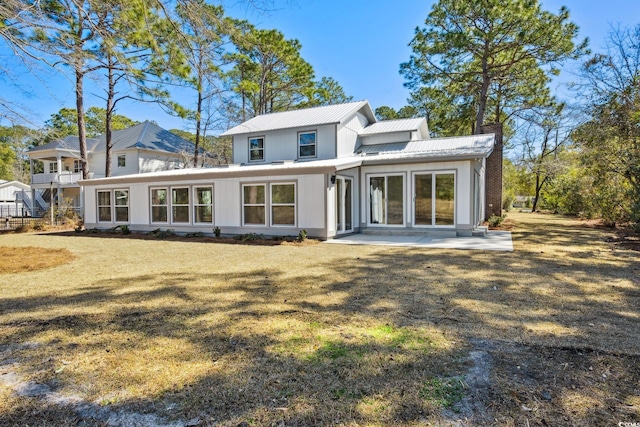 rear view of property with a patio, a chimney, metal roof, a standing seam roof, and a yard