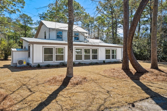 view of front facade with board and batten siding, ac unit, metal roof, and a front yard