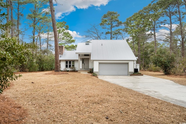 view of front of house with metal roof, a garage, driveway, stucco siding, and a chimney