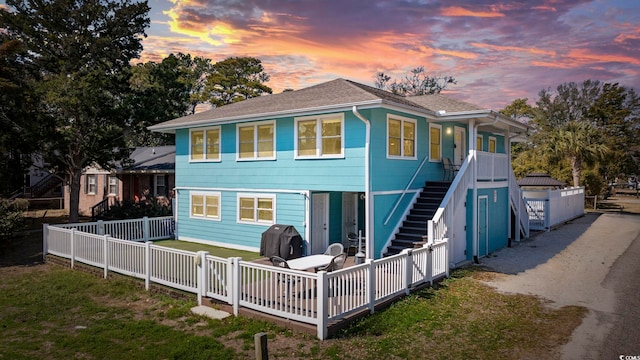 back of house at dusk with roof with shingles, stairway, a chimney, and fence