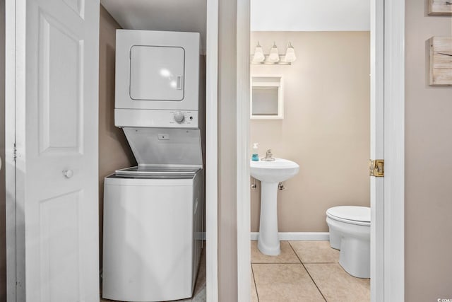 half bathroom featuring baseboards, a sink, toilet, stacked washing maching and dryer, and tile patterned flooring