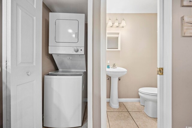 bathroom featuring stacked washer and dryer, baseboards, toilet, tile patterned flooring, and a sink