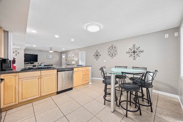 kitchen with stainless steel dishwasher, light tile patterned flooring, a sink, dark countertops, and baseboards