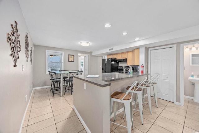 kitchen featuring light tile patterned floors, light brown cabinets, a peninsula, a breakfast bar, and black fridge