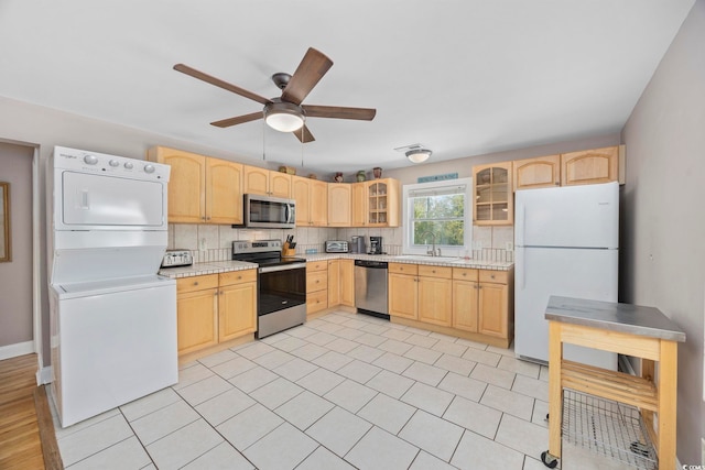 kitchen featuring stacked washer and dryer, light countertops, light brown cabinetry, appliances with stainless steel finishes, and a sink