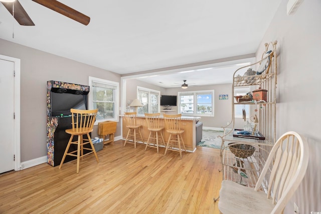 kitchen with a breakfast bar area, a peninsula, a ceiling fan, baseboards, and light wood finished floors