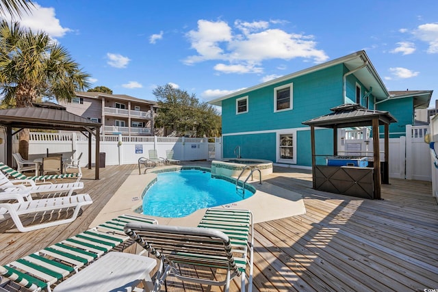 community pool featuring a gazebo, a wooden deck, a fenced backyard, and a hot tub