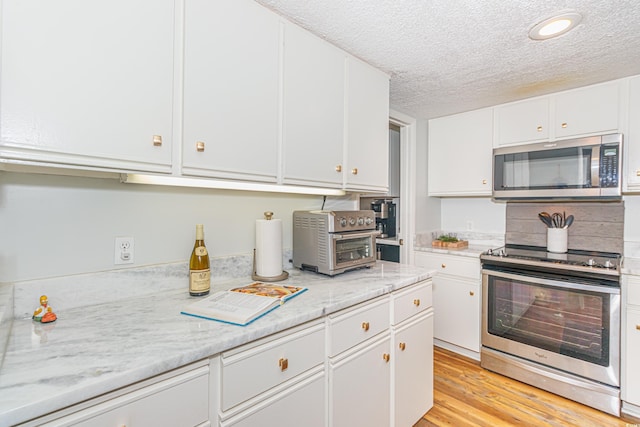 kitchen featuring a textured ceiling, a toaster, stainless steel appliances, white cabinetry, and light wood-type flooring