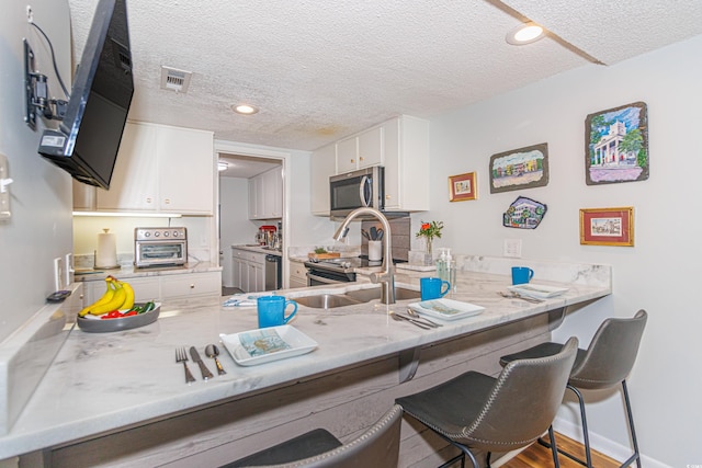 kitchen with stainless steel appliances, a peninsula, visible vents, and white cabinetry