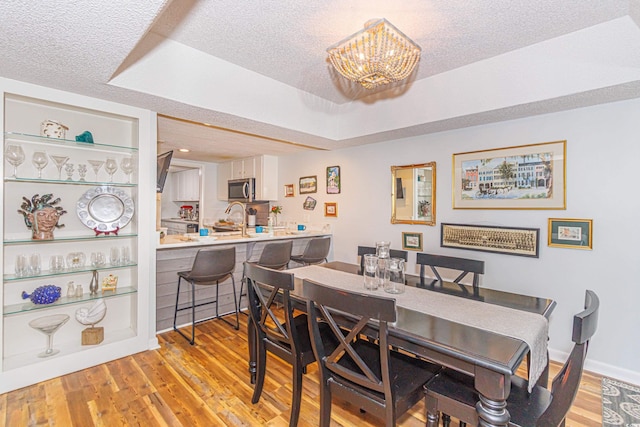 dining area with a textured ceiling, a raised ceiling, light wood-style flooring, and an inviting chandelier