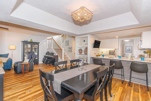 dining area with a textured ceiling, light wood finished floors, stairway, a tray ceiling, and an inviting chandelier