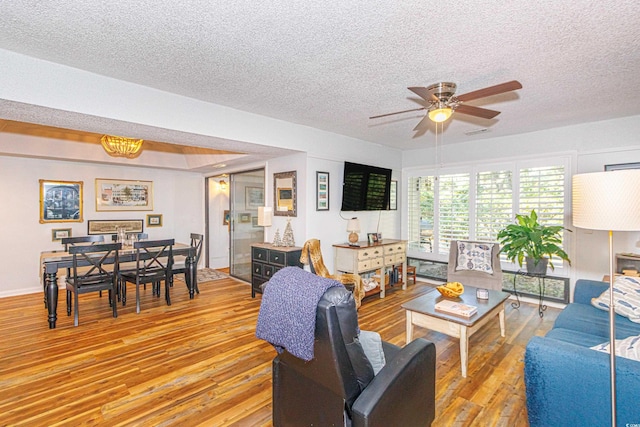 living area with light wood-type flooring, ceiling fan, and a textured ceiling