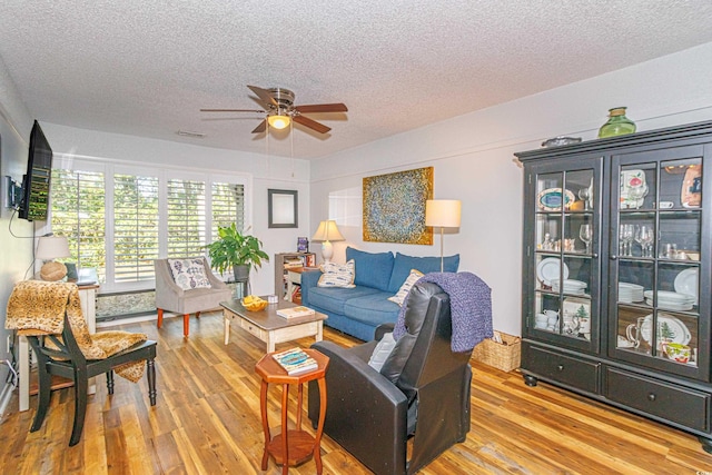 living area featuring visible vents, ceiling fan, a textured ceiling, and light wood finished floors